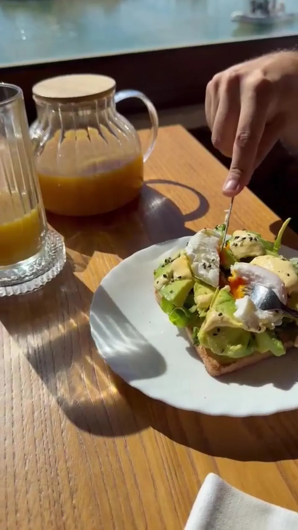 Avocado toast con uovo in camicia e caraffa di succo d'arancia davanti alla vetrata