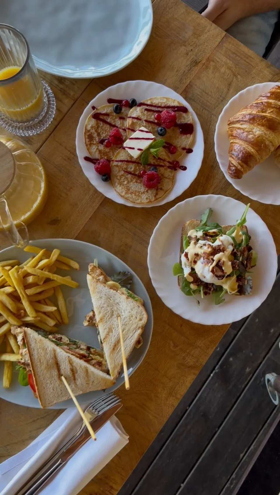 Un tavolo di brunch: pancake ai frutti di bosco, club sandwich con patatine, croissant e spremuta